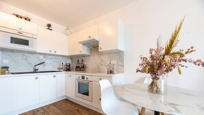 A modern kitchen with white cabinets, a marble countertop, and a dining area with a white table and chairs. - Occi - proche plage - One Bedroom Apartment, Sleeps 4 (L'Île-Rousse)