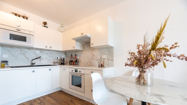 Une cuisine moderne avec des meubles blancs, un plan de travail en marbre et un coin repas comprenant une table et des chaises blanches.