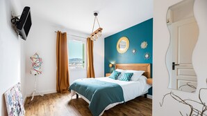 A bedroom with a bed, wooden floor, a TV mounted on the wall, and a window with curtains. - Occi - proche plage - One Bedroom Apartment, Sleeps 4 (L'Île-Rousse)