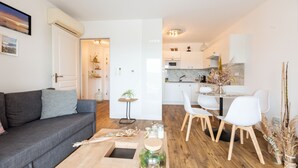 A modern living room with a grey sofa, a wooden coffee table, and a dining area with white chairs and a glass table. - Occi - proche plage - One Bedroom Apartment, Sleeps 4 (L'Île-Rousse)