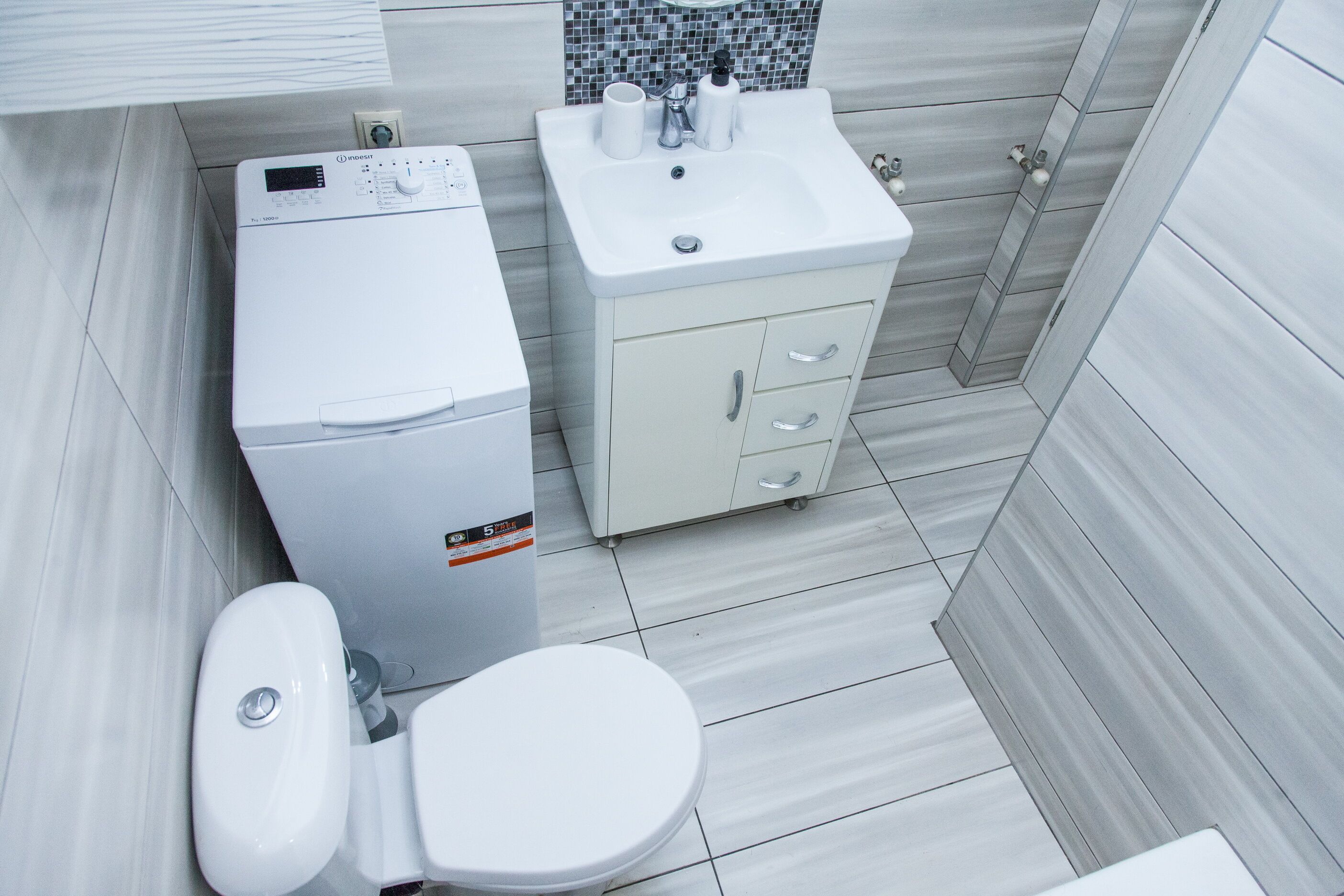 A modern bathroom with a white toilet, a washing machine, and a sink with a mirror.