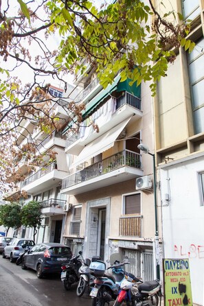 A multi-story residential building with balconies, parked cars, and a motorcycle. - Beautiful new decorated apt in Athens (Athens)