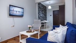 A modern living room with a blue sofa, a white coffee table, and a television mounted on the wall. - Beautiful new decorated apt in Athens (Athens)