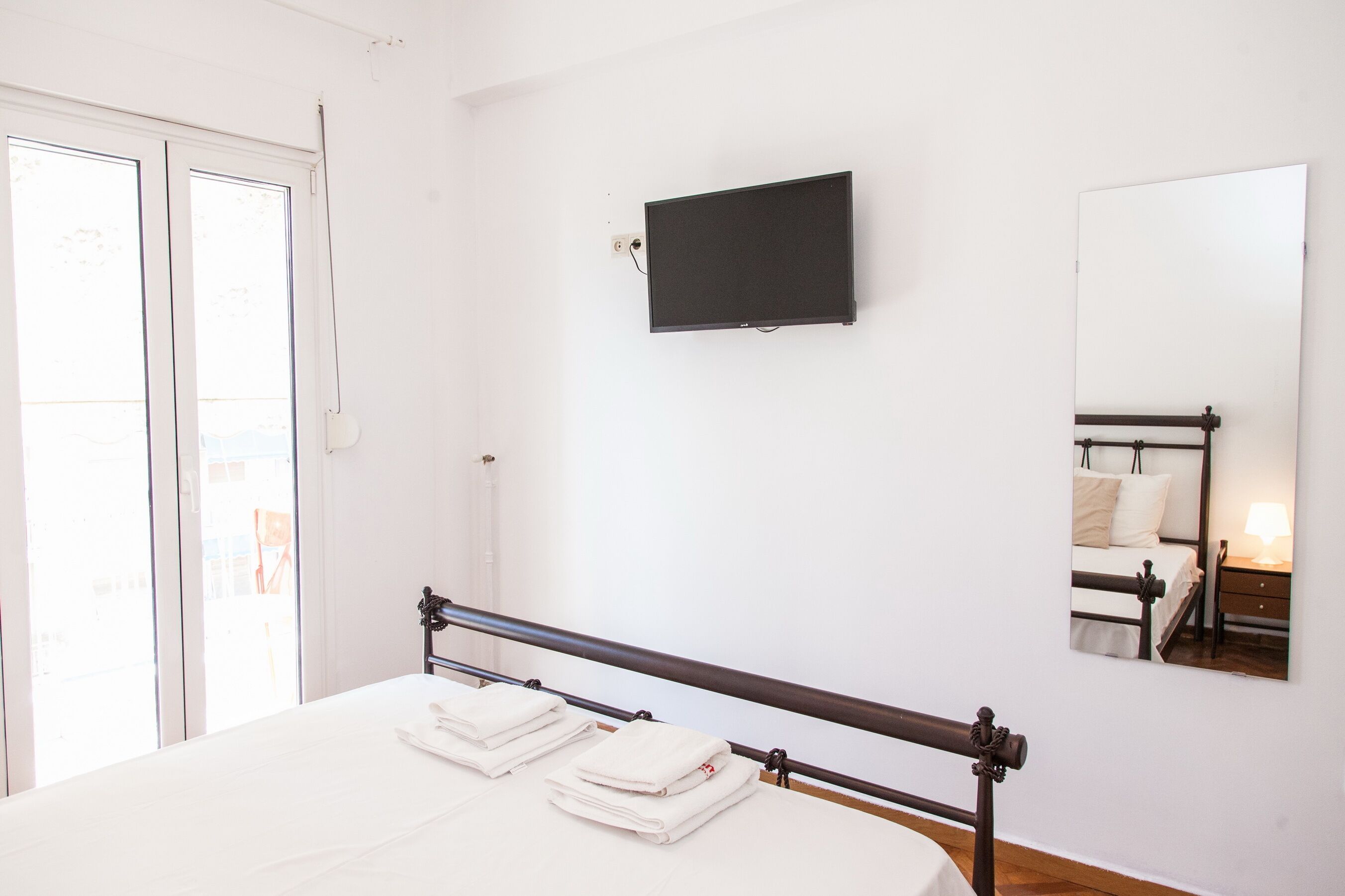 Una camera d'albergo con un letto, una televisione a schermo piatto montata a parete, uno specchio e una finestra con vista sull'esterno.