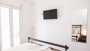 A hotel room with a bed, a flat-screen TV mounted on the wall, a mirror, and a window with a view of the outside. - Beautiful new decorated apt in Athens (Athens)