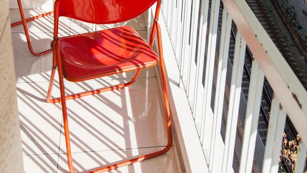 A balcony with two red chairs and a small table, overlooking a busy street with cars and buildings. - Beautiful new decorated apt in Athens (Athens)