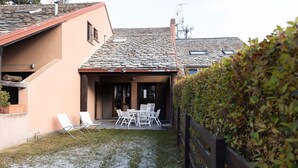 Ein Haus mit einem Stein-Dach, einer überdachten Terrasse mit Stühlen und einer Hecke.