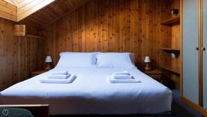 Ein Zimmer mit Holzwänden, einem Bett, zwei Nachttischen und einer Lampe auf jedem Tisch.