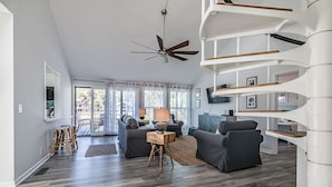 Ein großzügiges Wohnzimmer im modernen Stil, mit einer Wendeltreppe, einem Deckenventilator und einem großen Fenster mit Vorhängen.