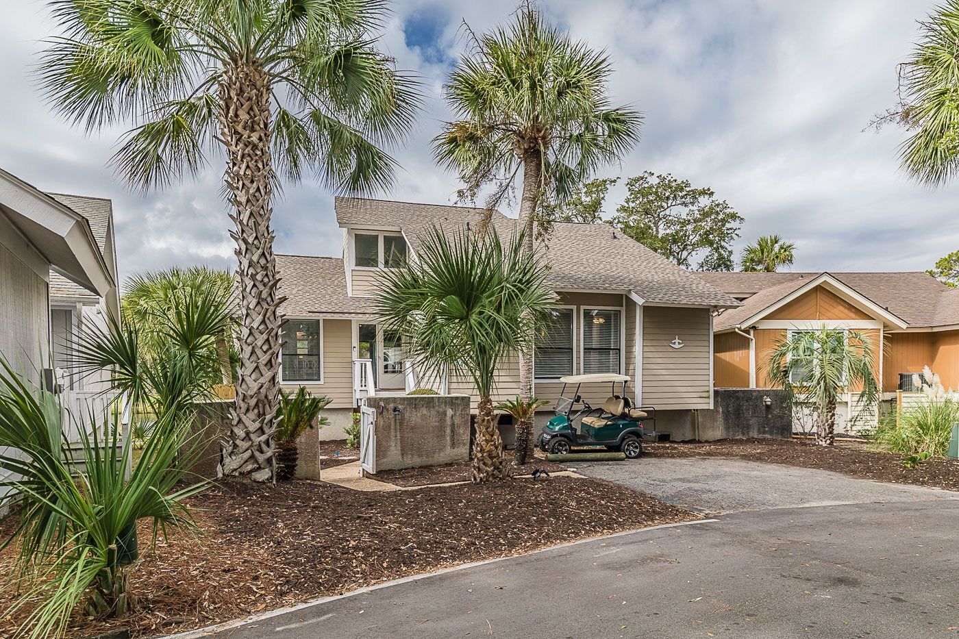 A two-story house with a garage, surrounded by palm trees and a golf cart.