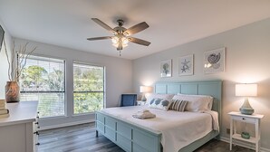 Ein Schlafzimmer mit Bett, Deckenventilator, Nachttisch mit Lampe und Bildern an der Wand.
