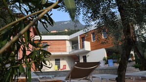 Un espace extérieur moderne, aménagé avec des tables en bois et des chaises en métal, offrant une vue sur un immeuble doté d’un balcon et sur une montagne en arrière-plan.