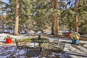 An outdoor seating area with metal chairs and a round table, surrounded by tall trees and a snowy ground. - 3 Mi to National Park: Cozy Studio in Grand Lake (Grand Lake)