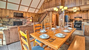 A spacious living area with a wooden dining table set for six, a stone fireplace, and a cozy sofa. - Lake Harmony Access: Home w/ Game Room + Fire Pit! (Lake Harmony)