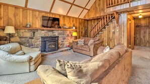A cozy living room with a stone fireplace, wooden walls, and a staircase leading to an upper level. - Lake Harmony Access: Home w/ Game Room + Fire Pit! (Lake Harmony)