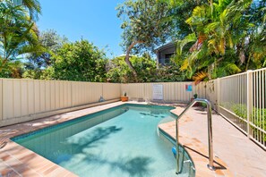 Une piscine dont le bord est revêtu de carrelage, entourée d’une clôture et d’une végétation luxuriante.