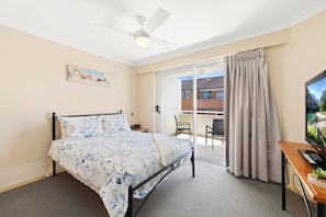 Een hotelkamer met een bed, een bureau met een computer, een plafondventilator en uitzicht op buiten.