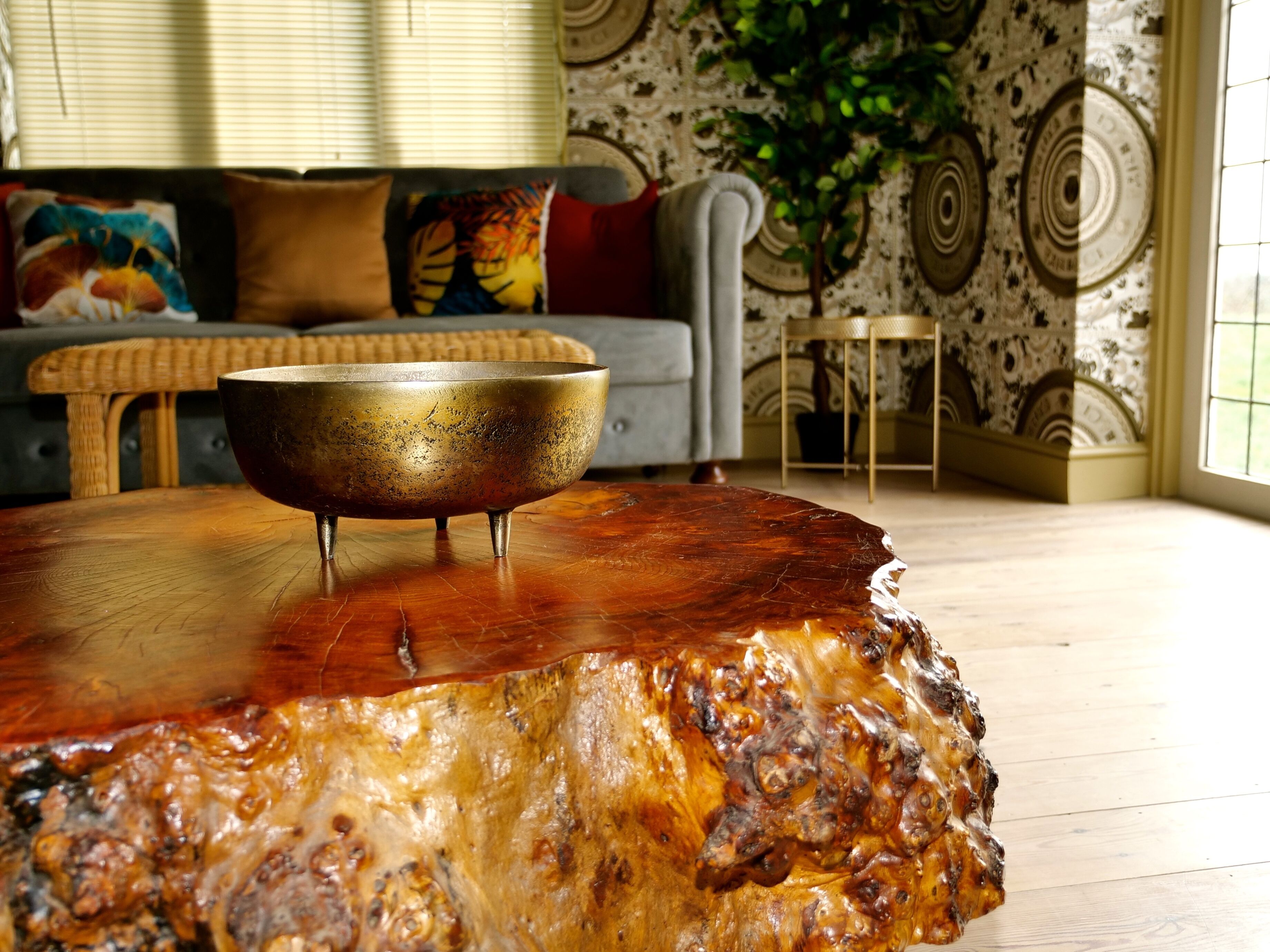 Een houten tafel met een bronzen kom, een grijze bank met kleurrijke kussens en een behang met patroon op de achtergrond.
