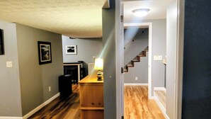 Un pasillo con piso de madera, una zona de cocina con mostrador y sillas, y una escalera que sube a otro nivel.