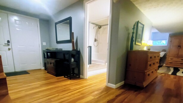 Una habitación amplia con piso de madera, una puerta blanca, un espejo y un aparador de madera.
