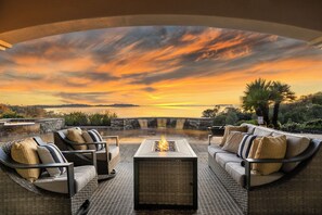Een terras in de open lucht met een vuurplaats, met uitzicht op een waterpartij en een zonsondergang.