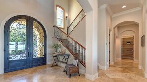 Un vestíbulo espacioso con una imponente escalera, un comedor con mesa y sillas, y un amplio arco de entrada.