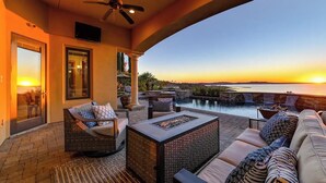 Un patio con mobiliario exterior, un ventilador de techo y vistas al atardecer sobre el agua.