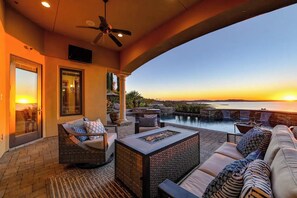 Un patio con posti a sedere all'aperto, una ventola a soffitto e vista sul tramonto sull'acqua.