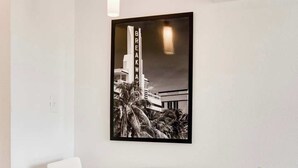 A modern dining area with a glass table and metal chairs, a black and white photograph on the wall, and an air conditioning unit above. - Best Beach Location | Wi-Fi, TV & Amenities (Miami Beach)