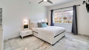 A bedroom with a bed, nightstands, a ceiling fan, a window with curtains, and a view of the outside. - Best Beach Location | Wi-Fi, TV & Amenities (Miami Beach)