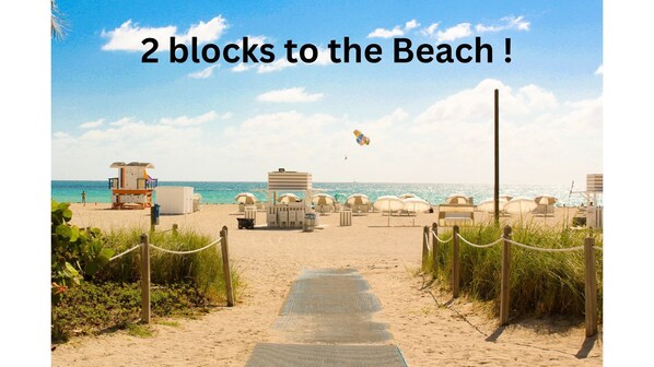 Stroll along the beach pathway to the shoreline, where a lifeguard tower and beach umbrellas offer a safe and shaded spot.