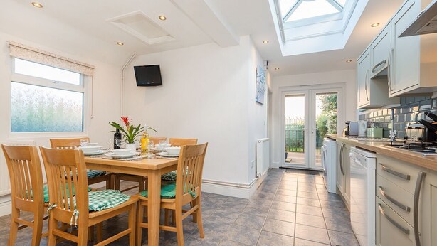 A modern kitchen with a dining area, featuring a skylight, white cabinets, and a tiled floor. - Augusta - cosy cottage near Sheringham town centre (Sheringham)