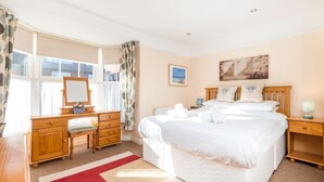 A hotel room with a large bed, a wooden dresser, a desk with a chair, and a window with curtains. - Augusta - cosy cottage near Sheringham town centre (Sheringham)