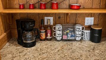 Una cocina con repisas de madera, un adorno de pez, tazas rojas, una cafetera y varias tazas con mensajes.