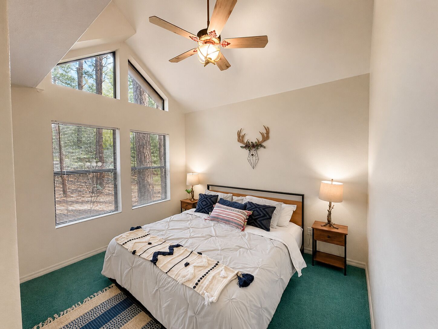A bedroom with a bed, a ceiling fan, a wall-mounted deer head decoration, and a window with blinds.