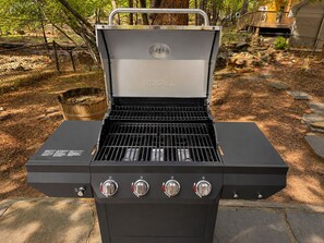 A black outdoor grill with four control knobs and a metal handle on top.