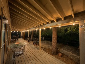 Una terraza exterior de madera con luces colgantes, una mesa de vidrio y sillas.