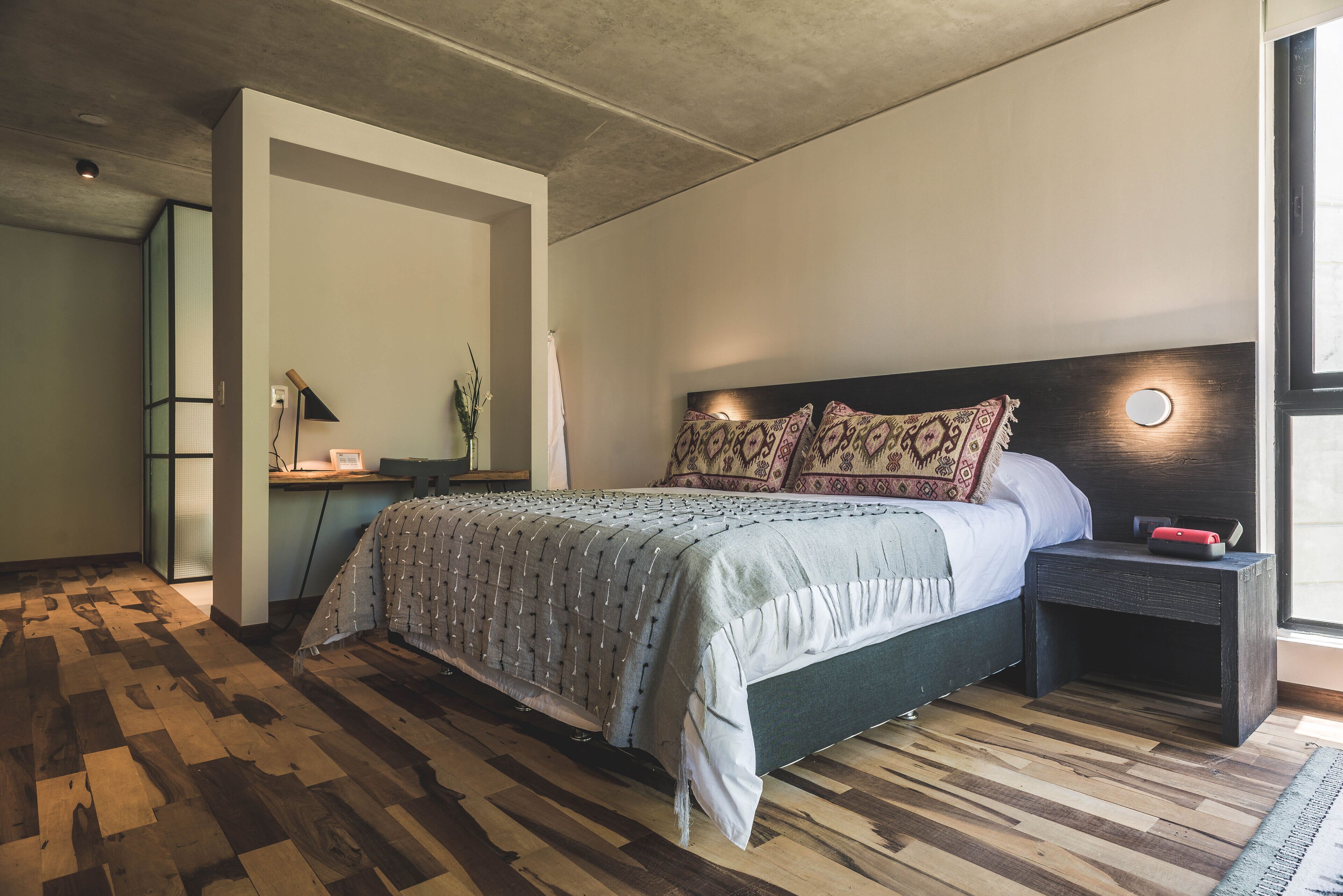 Un dormitorio con cama, mesita de noche y escritorio con lámpara.