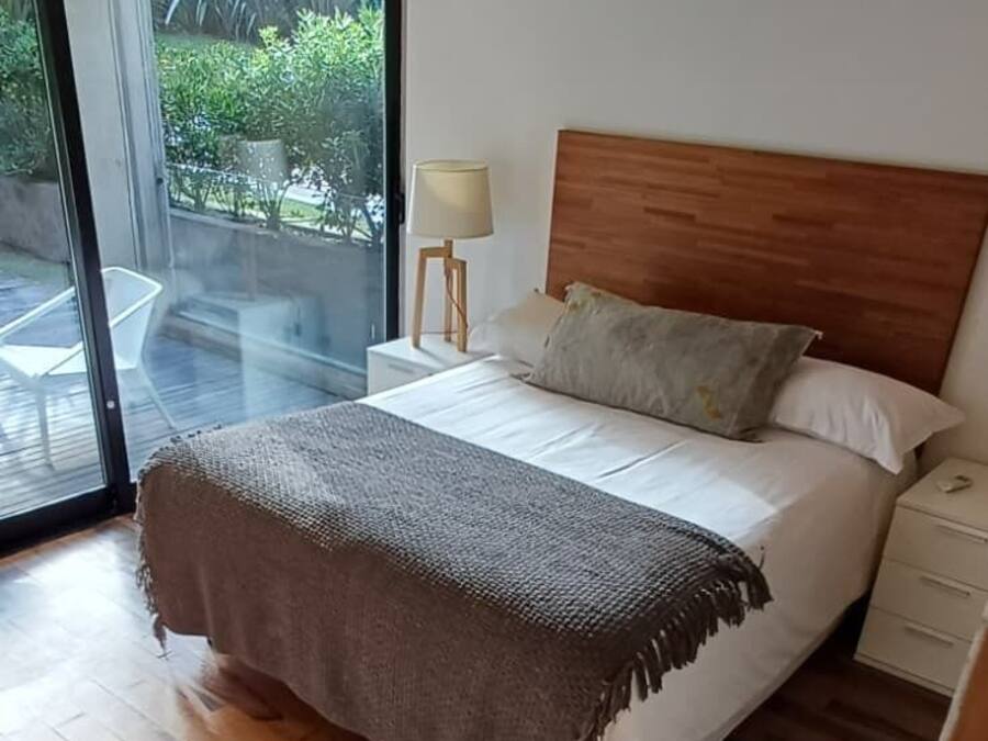 A bedroom with a bed, a nightstand, a lamp, and a view through a glass door to an outdoor area.