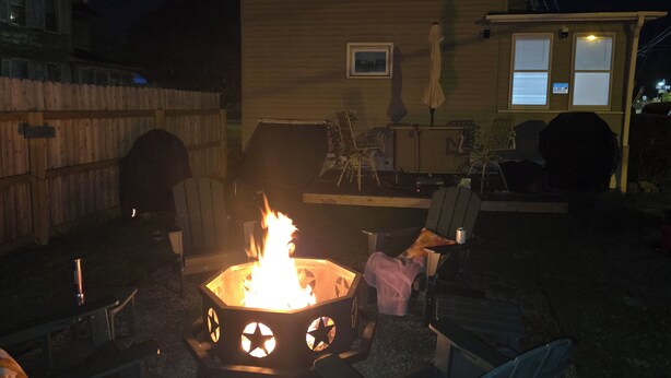 Ein Garten mit einem sechseckigen Feuerkorb, Gartenmöbeln und einem Holzzaun.