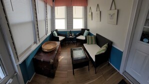 Ein gemütliches Zimmer mit einer Couch, Stühlen, einem kleinen Tisch und einem Fenster mit Jalousien.