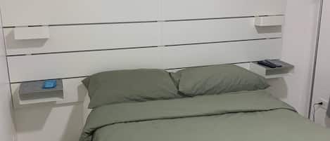 A small, neatly arranged bedroom with a single bed, a bedside table, and a nightstand.