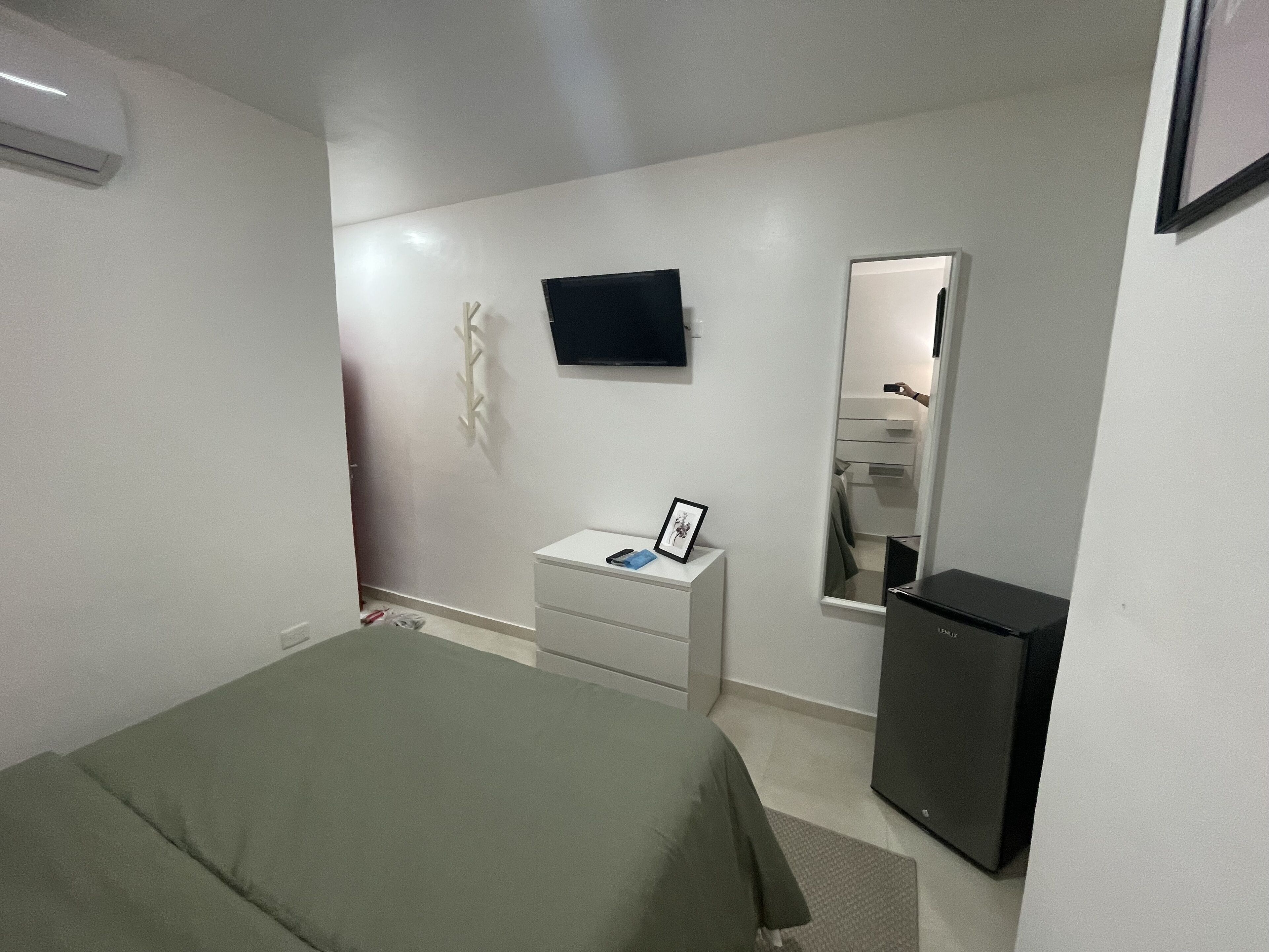 A bedroom with a bed, a dresser, a mirror, a television, and a refrigerator.