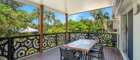 A covered outdoor area with a table and chairs, surrounded by a decorative fence, overlooking a lush garden.