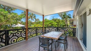 A covered outdoor area with a table and chairs, surrounded by a decorative fence, overlooking a lush garden.