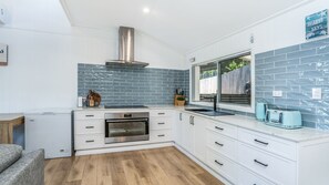 A modern kitchen with white cabinetry, a stainless steel oven, and a blue-tiled backsplash. - Castaway Cottage - Rainbow Beach (Rainbow Beach)