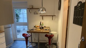A compact kitchen with a dining table, two red bar stools, a pendant light, and a calendar on the wall.