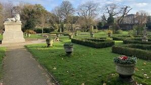 A formal garden with a central pathway, statues, and neatly trimmed hedges.