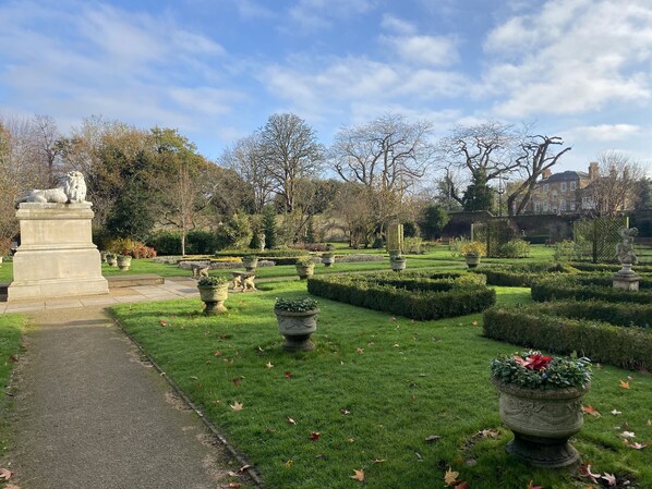 A formal garden with a central pathway, statues, and neatly trimmed hedges.