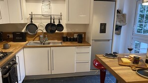 A modern kitchen with white cabinets, a red bar stool, and a window with a view of trees.